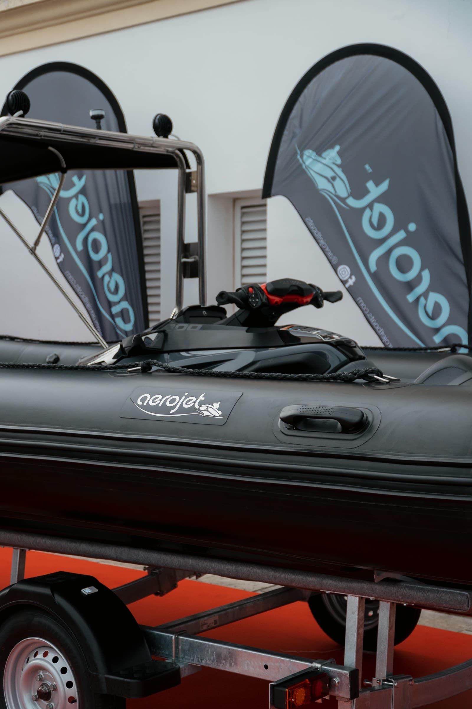 Aerojet με σκούρους σωλήνες και jet ski κουμπωμένο, πάνω στο τρέιλερ του, σε έκθεση σκαφών